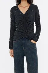 Camiseta negra de corte ajustado con escote pico y manga larga ajustada y fruncida. Presenta túneles fruncidos en delantero y espalda, y strass por toda la prenda.