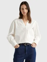 Blusa blanca de algodón orgánico con cuello en V, mangas largas abullonadas con puños abotonados y detalles de encaje vertical.