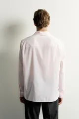 Camisa de corte regular fit color rosado pálido, con cuello solapa, manga larga y cierre frontal de botones.