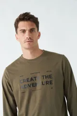 Remera verde militar de manga larga con cuello redondo y estampado frontal con la frase "Create the adventure".