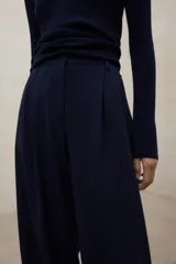 Pantalón negro de tiro alto, corte ancho y pierna recta, con pliegues frontales.