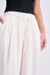 Pantalón de lino blanco de corte amplio, con cintura alta y lazo marrón con flecos.