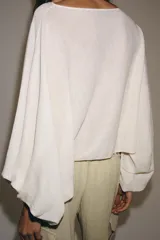 Cuerpo de punto color crudo, con cuello barco y mangas largas abullonadas con sisa ancha y puños ajustados.