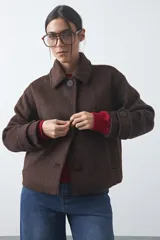 Tapado corto de paño con textura, color marrón, de corte recto y silueta estructurada. Presenta cuello camisero, cierre frontal con botones grandes y mangas largas con detalle de trabas en los puños.
