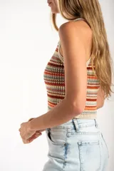 Top tejido de punto con diseño a rayas horizontales en tonos tierra, naranja y crema. Presenta un corte al cuerpo, escote halter y breteles finos.