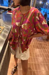 Blusa de lino bordado con estampado floral en tonos fucsia, marrón y blanco, de calce holgado, escote en V con cordones para atar y mangas cortas abullonadas.