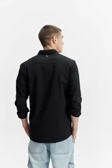 Camisa de manga larga color gris oscuro, confeccionada en tejido liviano con textura sutil, cuello tradicional y cierre frontal de botones.