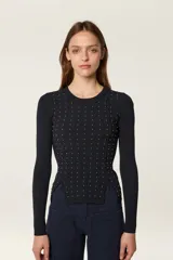 Sweater de punto fino en color negro, con diseño de canalé, cuello redondo y mangas largas. Presenta un corte ajustado con aberturas laterales en el ruedo y está decorado con pequeñas cuentas doradas en la parte frontal.