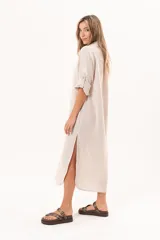 Vestido camisero largo de lino color beige, con silueta relajada, abotonado al frente, cuello camisero, mangas regulables y tajos laterales.