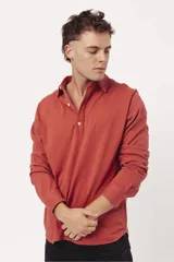 Buzo de algodón tipo polo con cuello camisero, cierre frontal con botones y mangas largas. Presenta un diseño liso en color terracota con logo bordado sutil en el pecho.