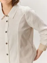 Camisa de lino color blanco con detalles combinados en tonos beige, cuello camisero, cierre frontal con botones oscuros y mangas largas con puños en contraste.