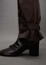 Pantalón de vestir de corte wide leg en color marrón, con diseño de tiro medio, detalle de pinzas frontales, bolsillos laterales y cierre frontal con cremallera, gancho y doble botón.