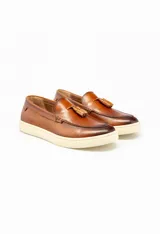 Mocasín de cuero color marrón con suela de goma color crema y detalle de pompón en la capellada.