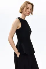 Chaleco negro de punto acanalado, sin mangas, con cuello redondo y cierre frontal de botones. Presenta un diseño entallado con bajo en peplum.