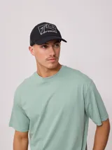 Gorra tipo trucker color negro con panel frontal de lona y malla trasera. Presenta estampado gráfico blanco con el logo de la marca en el frente.