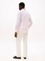 Camisa de hombre Tommy Hilfiger de manga larga a rayas verticales rosas y blancas, confeccionada en algodón regenerativo elástico. Tiene corte slim fit, cuello clásico, cierre con botones, puños abotonados y logo bordado en el pecho.