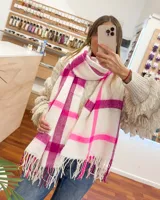 Bufanda rectangular de tejido suave color blanco con estampado de cuadros grandes en tonos fucsia y rosa. Tiene flecos en los extremos.