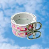 Cinturón de cuero vacuno en color marfil con diseño pintado a mano en tonos rosados, amarillos y blancos, de la marca Carolina De Cunto. Cuenta con herraje metálico ovalado en color oro viejo con logo grabado.