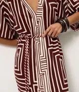 Vestido largo de viscosa con estampado geométrico en tonos bordó y blanco, escote en V y mangas cortas. Incluye un cinturón de cuerda para ajustar la cintura y una abertura frontal.
