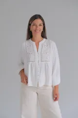 Blusa blanca de manga larga con cuello mao y cierre frontal con botones. Presenta detalles de bordado inglés y calados en la parte superior delantera.
