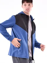 Campera deportiva con cierre frontal, capucha y diseño de bloques de color. La parte superior (hombros y capucha) es negra, y el cuerpo y mangas son de color azul vibrante, con un corte diagonal que separa ambos colores.