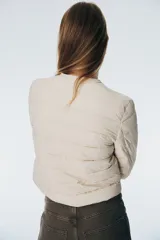 Campera acolchada de nylon color beige, con cuello redondo, cierre de botones a presión y bolsillos laterales discretos. Tiene elástico fino en los puños y está forrada.