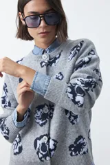 Cardigan de tejido jacquard color marrón con estampado floral en tonos rojo y rosado. Presenta cuello redondo, cierre frontal con botones y terminaciones acanaladas en puños y ruedo.