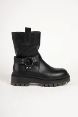 Bota biker color negro de símil cuero, con suela tipo plataforma chunky y taco cuadrado. Presenta una tira con tachas metálicas y una argolla que rodea el tobillo, además de una presilla en la parte superior de la caña.