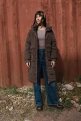 Campera larga acolchonada color marrón, con diseño midi, capucha amplia, cierre frontal con cremallera y broches, y bolsillos delanteros con tapa.