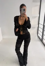 Conjunto de dos piezas compuesto por top de manga larga con cierre frontal de lazos y pantalón de corte acampanado. Ambas prendas están confeccionadas en encaje negro con diseño de franjas horizontales superpuestas.