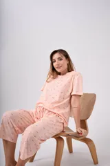 Pijama capri de algodón coral con pequeño estampado floral multicolor, compuesto por una remera de manga corta con escote redondo y botones frontales, y un pantalón capri con cintura elástica.