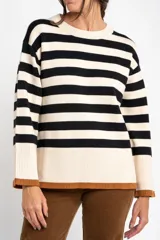 Sweater de punto con diseño a rayas horizontales en color negro y crema, de corte oversize. Presenta cuello redondo, mangas largas con puños acanalados y un detalle de borde inferior en color cobre con acabado brillante.