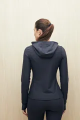 Campera deportiva negra de calce entallado, con cierre frontal completo, capucha integrada y mangas largas con puños envolventes. Presenta costuras estratégicas que estilizan la silueta y bolsillos laterales funcionales.