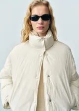 Campera acolchada de nylon color crema, con diseño oversize, cuello alto y cierre frontal con botones a presión. Cuenta con mangas largas y bolsillos laterales.