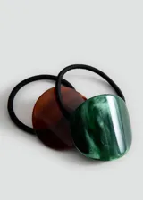Pack de dos gomas de pelo elásticas con apliques decorativos de resina y acetato, uno circular en tonos marrones y otro ovalado en tonos verdes.
