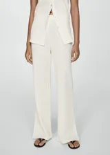 Pantalon de crochet color crema, de corte recto y tiro alto con cintura elástica. Presenta un diseño de tejido calado con aberturas laterales en el bajo.