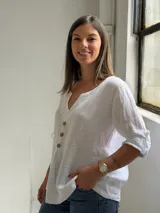 Blusa blanca de lino, con escote en V y tres botones frontales grandes de madera. Cuenta con mangas tres cuartos con presilla y botón para arremangar.