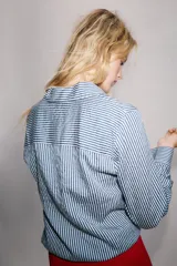 Camisa de cuello solapa y manga larga, con bajo ajustable mediante cordones y cierre frontal con botones ocultos. Diseño a rayas blancas y azules.