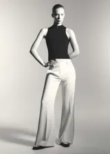 Pantalon de corte wideleg en color beige, confeccionado en tejido fluido. Presenta diseño de rayas laterales en contraste, trabillas para cinturón, dos bolsillos laterales y cierre oculto de botón, gancho y cremallera.