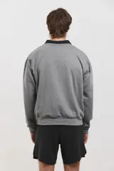 Buzo de algodón rústico color gris melange, con cuello redondo y cuello tipo polo negro superpuesto. Presenta el logo de la marca bordado en el pecho y puños acanalados.