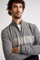 Sweater de tejido de punto con diseño color block en tonos gris, gris claro y negro. Presenta cuello levemente elevado con cierre frontal parcial, mangas largas con puños acanalados y logo bordado en el pecho.
