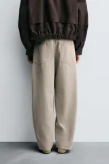 Pantalón de algodón color beige, estilo wide balloon fit, con cintura ajustable mediante cinturón de la misma tela. Presenta bolsillos frontales y bolsillos traseros de plastrón, con efecto lavado y abertura en el bajo.