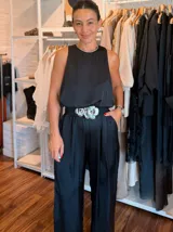 Mono largo de satén negro con cuello redondo adornado con pedrería brillante. Presenta un diseño sin mangas, cintura elástica con un cinturón decorativo de flores metálicas y pantalones de corte recto con bolsillos laterales.