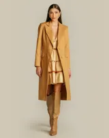 Gabardina larga color camel, estructurada, con solapa clásica, hombros marcados, cierre frontal con botones y bolsillos con solapa.