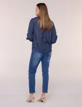 Camisa de estilo boho, color verde, con cuello camisero, escote en V y botonadura frontal con botones perlados. Cuenta con una pechera con bordados geométricos y florales a contraste, mangas largas abullonadas con puños abotonados y delicados bordados dispersos.