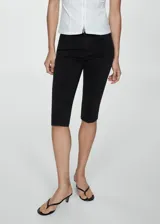 Pantalón tipo capri de denim negro con corte skinny, tiro medio, cierre de cremallera y botón, y costuras decorativas verticales en el frente.