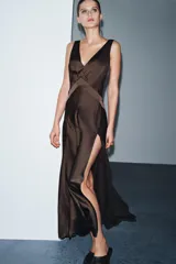 Vestido largo de satén color marrón oscuro, con escote en pico pronunciado, tirantes anchos y bajo en línea evasé con abertura lateral.