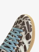 Championes Adidas modelo Handball Spezial W, con estampado animal print tipo vaca en tonos marrones y blancos, tiras laterales blancas, cordones celestes y suela de goma translúcida.