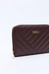 Billetera capitoneada en símil cuero color negro, con pespuntes en diagonal y cierre perimetral. Cuenta con un logo metálico dorado en el frente.