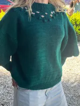 Sweater tejido a mano de lana merino color verde oscuro, con cuello alto, mangas abullonadas y detalle de bordado floral artesanal en el canesú.